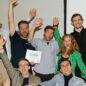 group of eleven people cheering on the winner