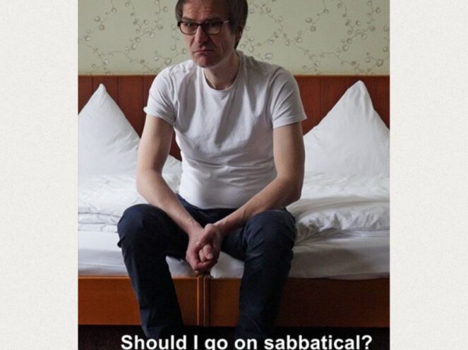 A contemplative image of a man seated on the edge of a neatly made bed in a modestly decorated room. He is wearing a white t-shirt and dark pants, leaning slightly forward with his hands clasped, appearing deep in thought. The caption at the bottom reads,