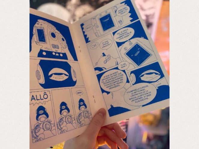 A close-up of an open comic book held by a hand, featuring bold blue and white illustrations. The panels depict a narrative involving a robot and a conversation written in French, with speech bubbles exploring technological and human interactions. The robot's design is whimsical, with large, expressive features. The background is softly blurred, emphasizing the comic's details and creating a warm, inviting atmosphere. The scene conveys creativity, storytelling, and a focus on futuristic themes.