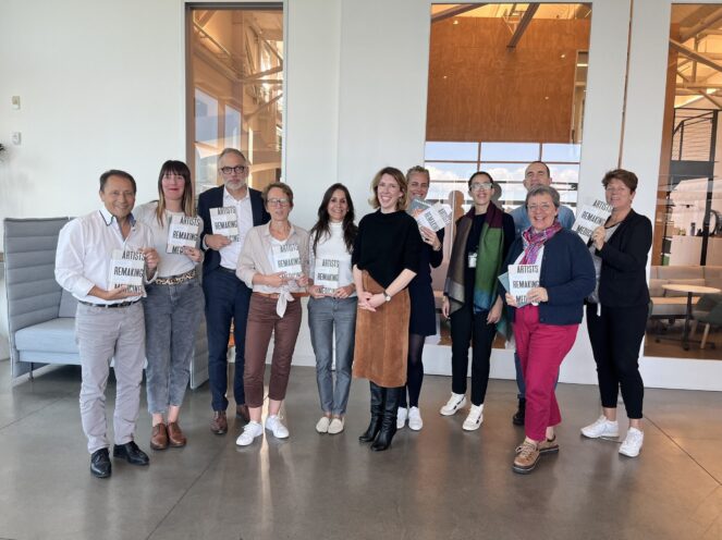 A group of people standing in a bright, modern interior space. They are holding books titled 