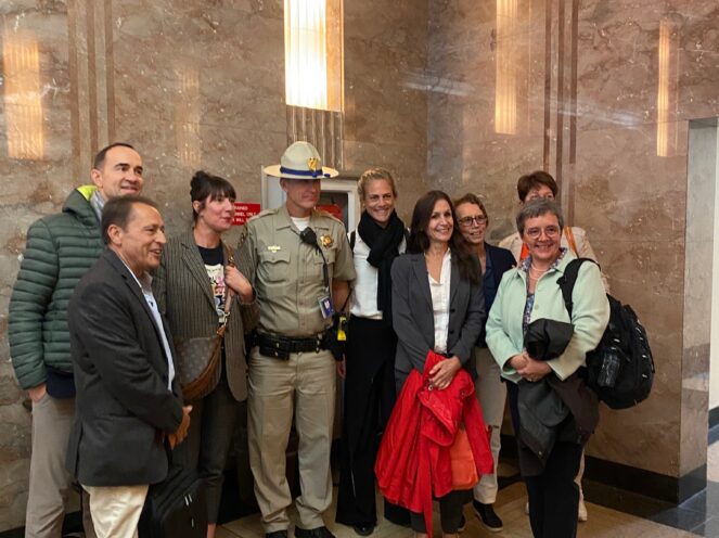 A group of individuals posing with a uniformed officer in an interior space with marble walls and warm lighting. The group appears to be engaged and enjoying the setting.